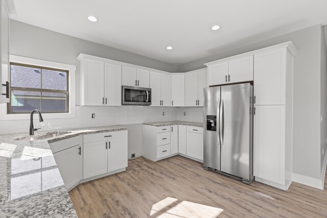 kitchen featuring sink, appliances with stainless steel finishes, white cabinetry, light hardwood / wood-style floors, and light stone countertops