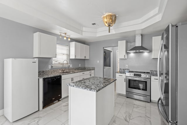 kitchen featuring sink, appliances with stainless steel finishes, white cabinetry, a center island, and wall chimney exhaust hood