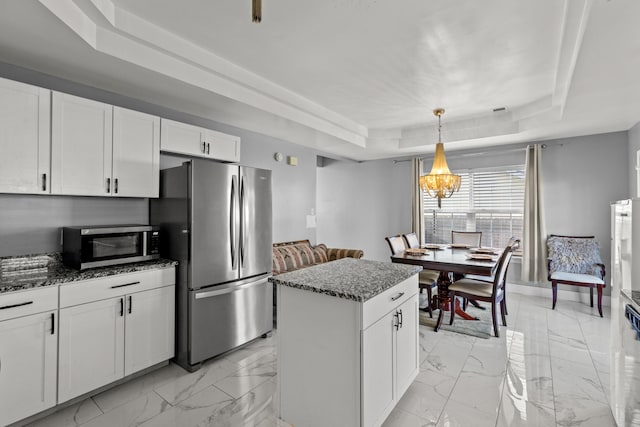 kitchen with decorative light fixtures, a center island, a tray ceiling, stainless steel appliances, and white cabinets