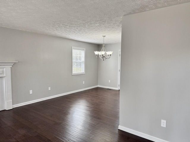 unfurnished dining area featuring dark wood-type flooring, a textured ceiling, a notable chandelier, and baseboards