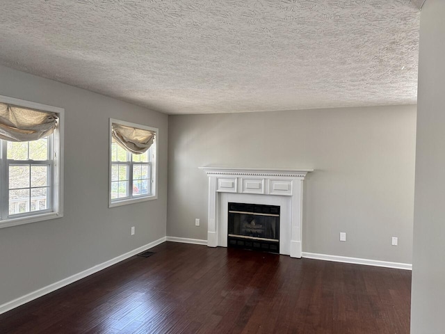 unfurnished living room with dark wood-style flooring, baseboards, a fireplace, a textured ceiling, and visible vents