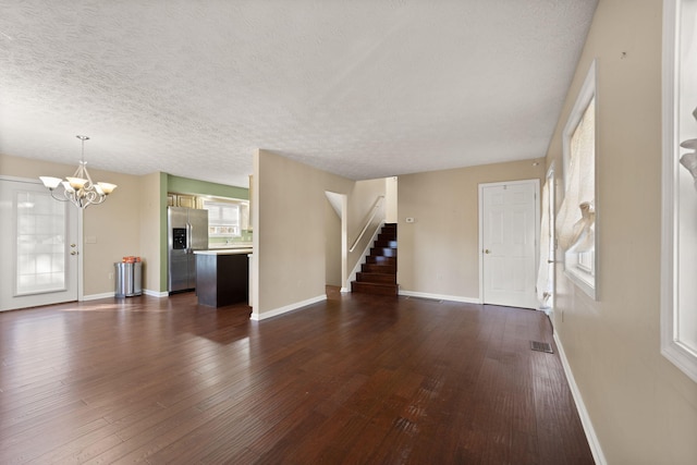 unfurnished living room with a notable chandelier, dark hardwood / wood-style floors, and a textured ceiling