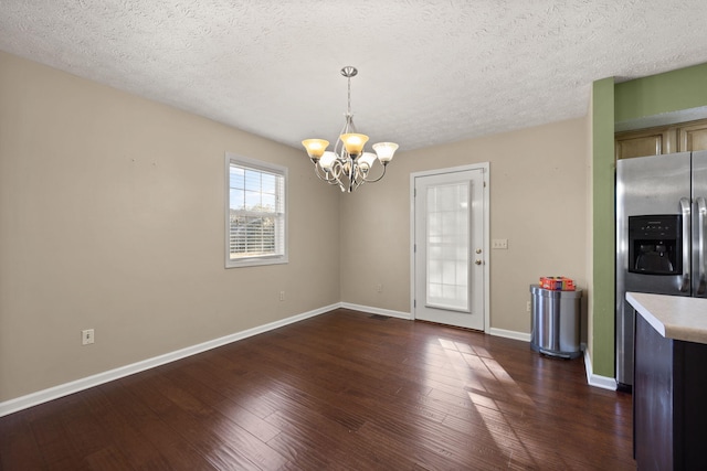 unfurnished dining area with an inviting chandelier, dark hardwood / wood-style floors, and a textured ceiling