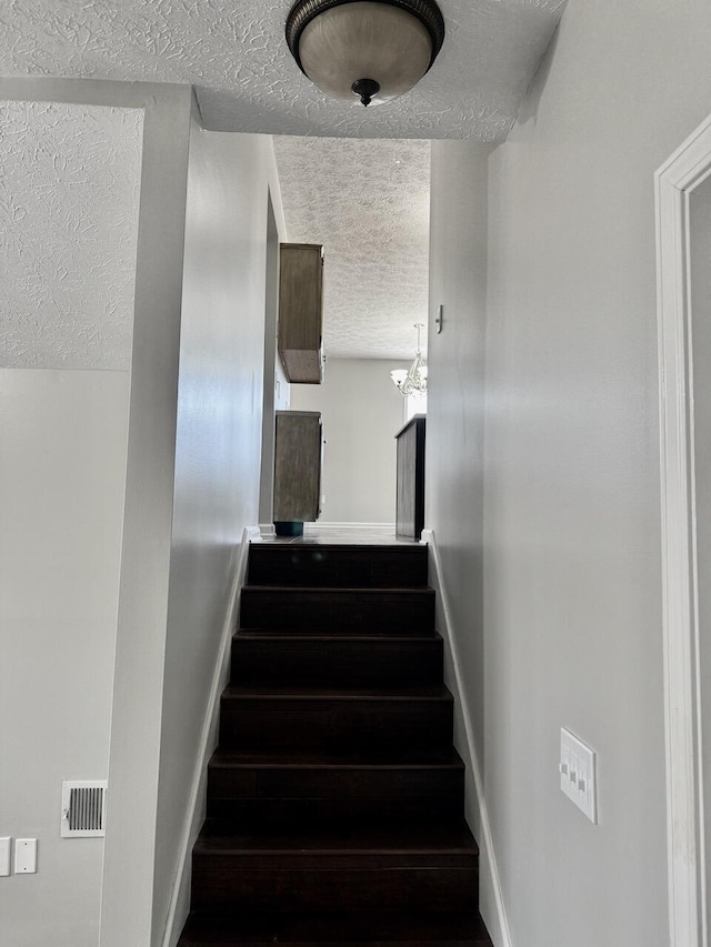 staircase with visible vents, a textured ceiling, baseboards, and wood finished floors