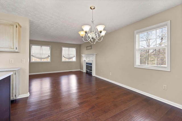 unfurnished living room featuring plenty of natural light, dark hardwood / wood-style floors, a textured ceiling, and an inviting chandelier