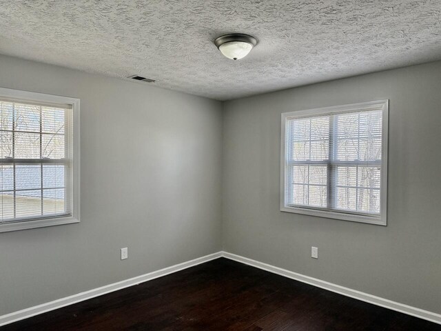 unfurnished room with a textured ceiling, baseboards, dark wood-style floors, and visible vents