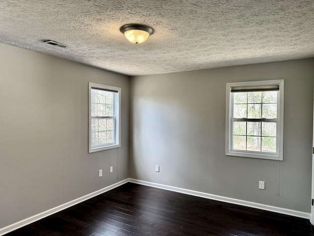 empty room featuring dark wood-style flooring, visible vents, baseboards, and a textured ceiling