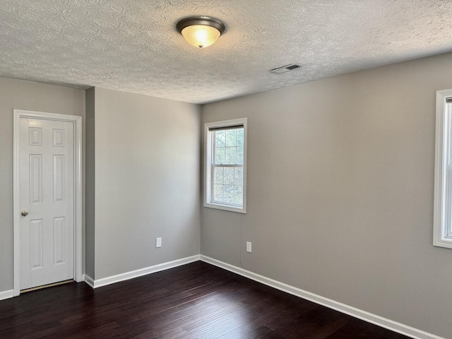 empty room with visible vents, baseboards, a textured ceiling, and dark wood finished floors