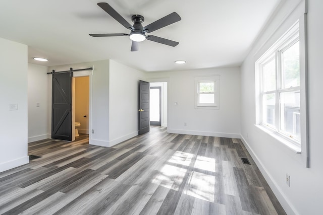 unfurnished room featuring a barn door, dark hardwood / wood-style floors, and ceiling fan