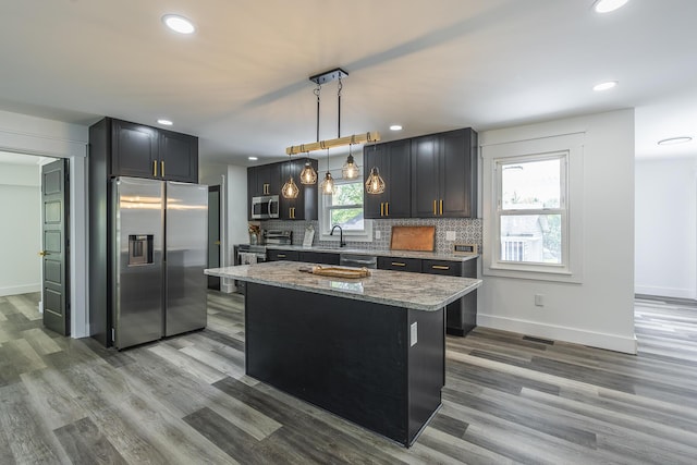 kitchen featuring appliances with stainless steel finishes, a kitchen island, a wealth of natural light, hanging light fixtures, and light stone countertops