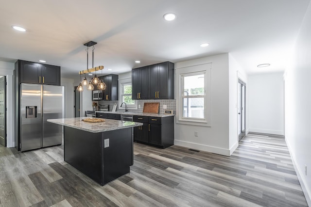 kitchen featuring appliances with stainless steel finishes, backsplash, a center island, light stone countertops, and decorative light fixtures