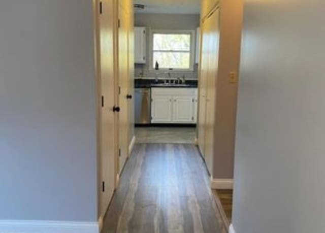 hallway featuring dark wood-style flooring, a sink, and baseboards