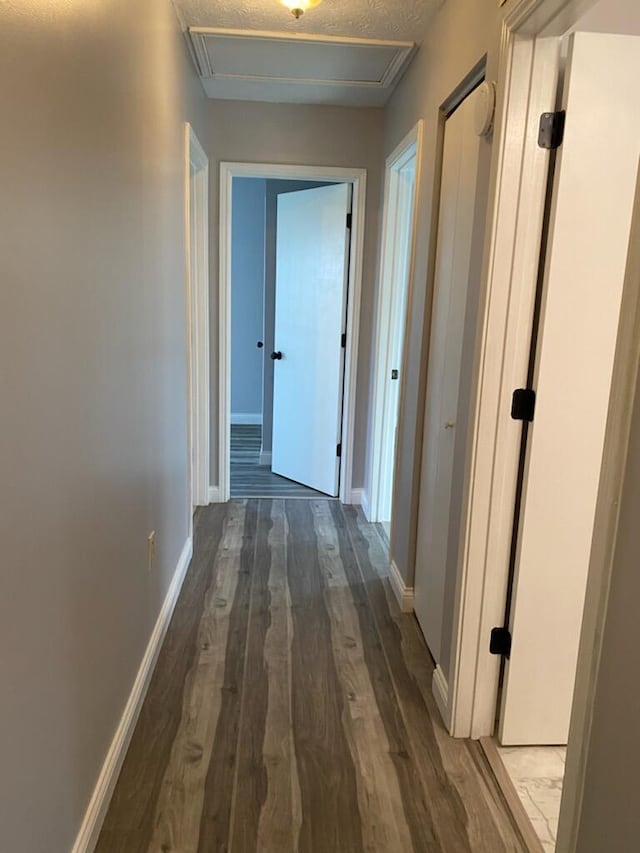 hallway with a textured ceiling, baseboards, and wood finished floors