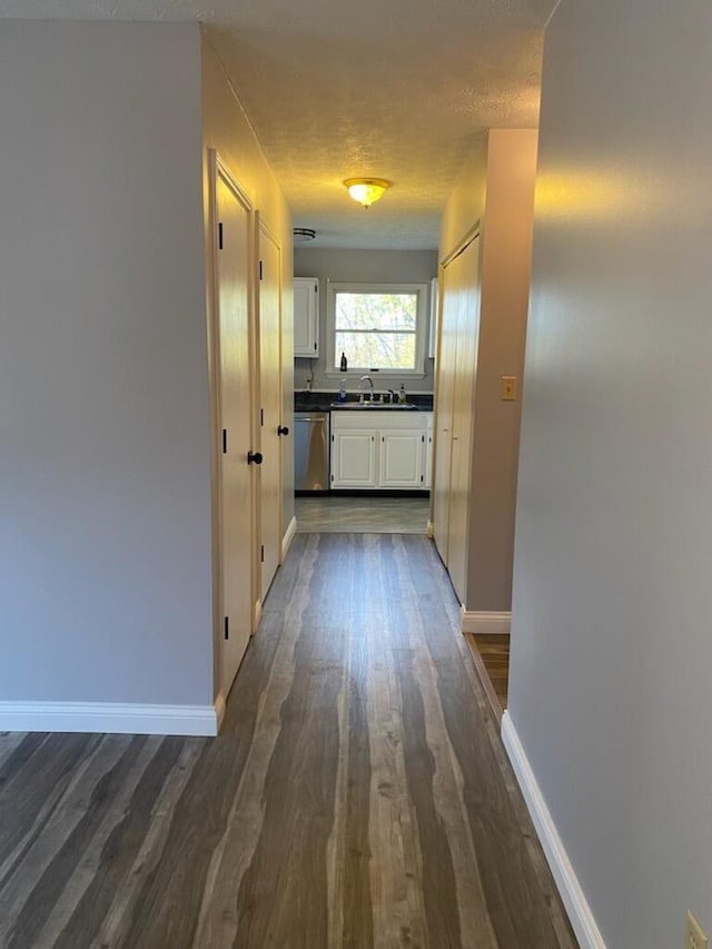 hall with a sink, a textured ceiling, baseboards, and dark wood-style flooring