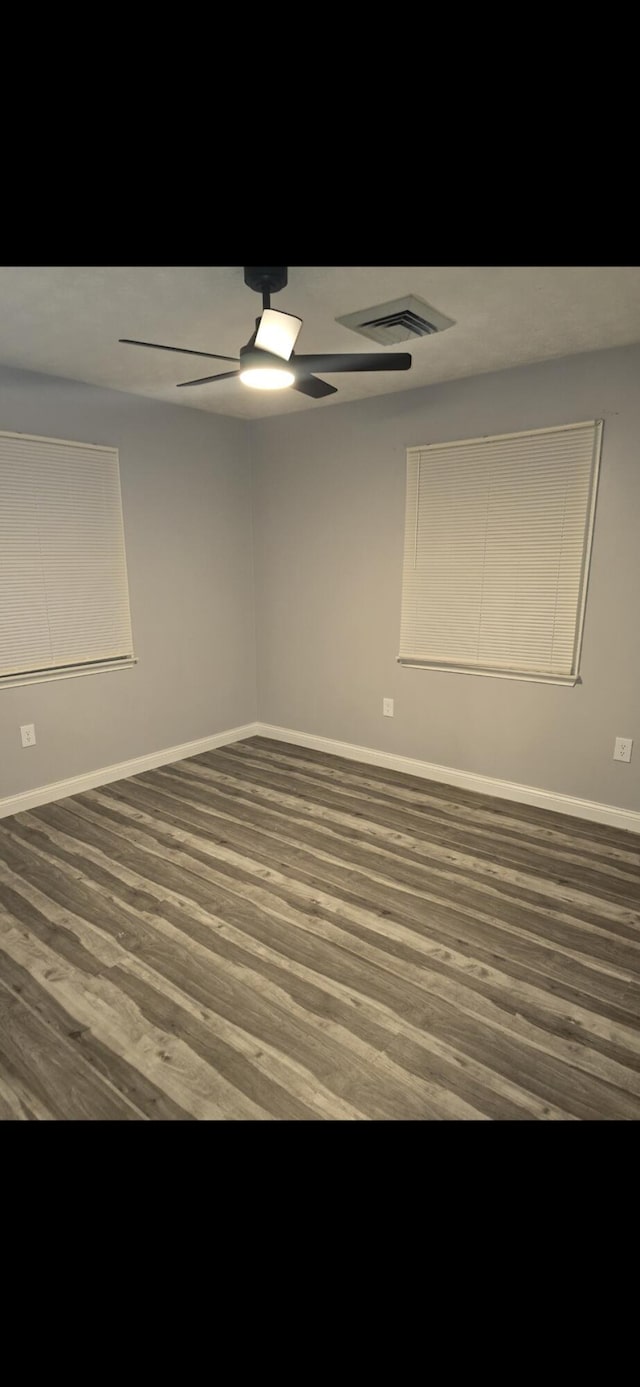 unfurnished room with a ceiling fan, visible vents, baseboards, and wood finished floors