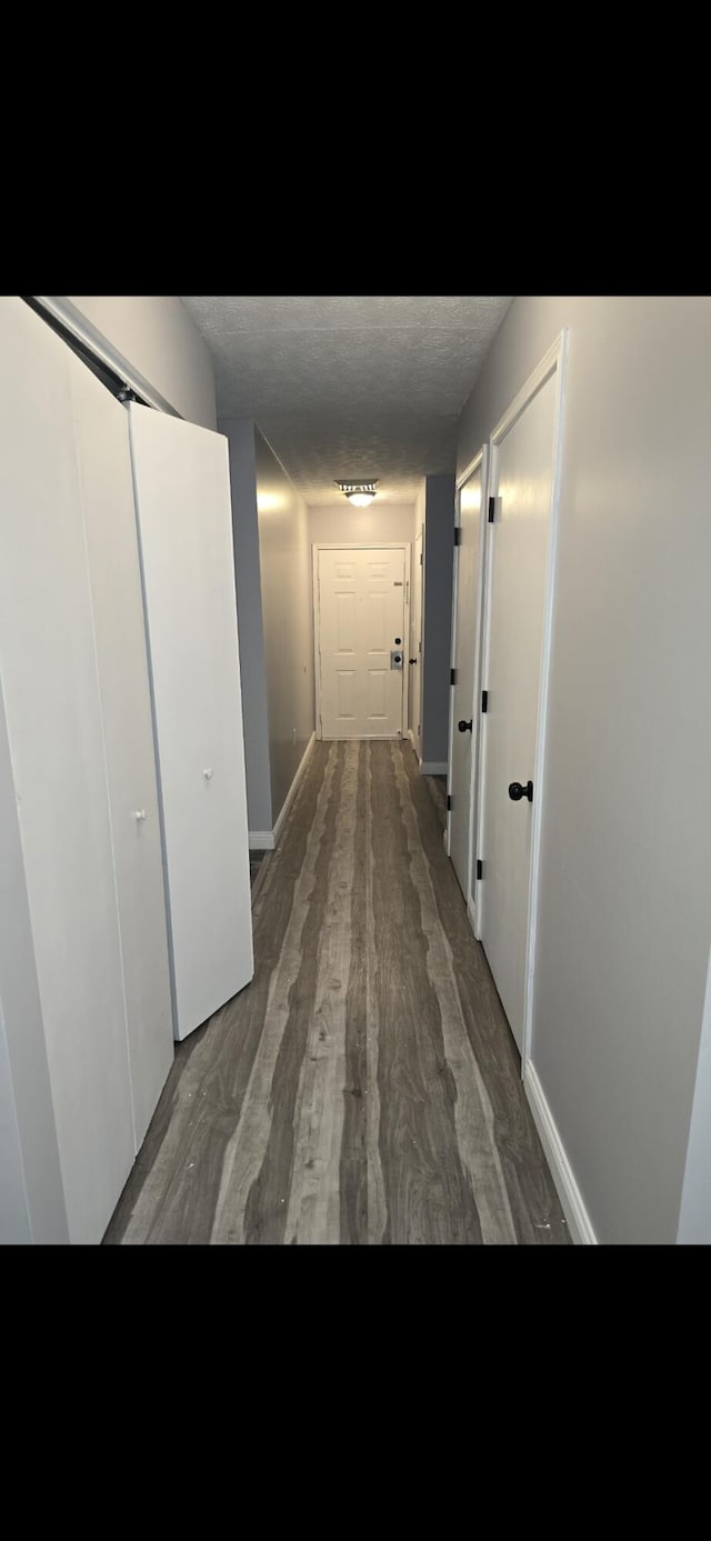 hall with a textured ceiling, baseboards, and wood finished floors