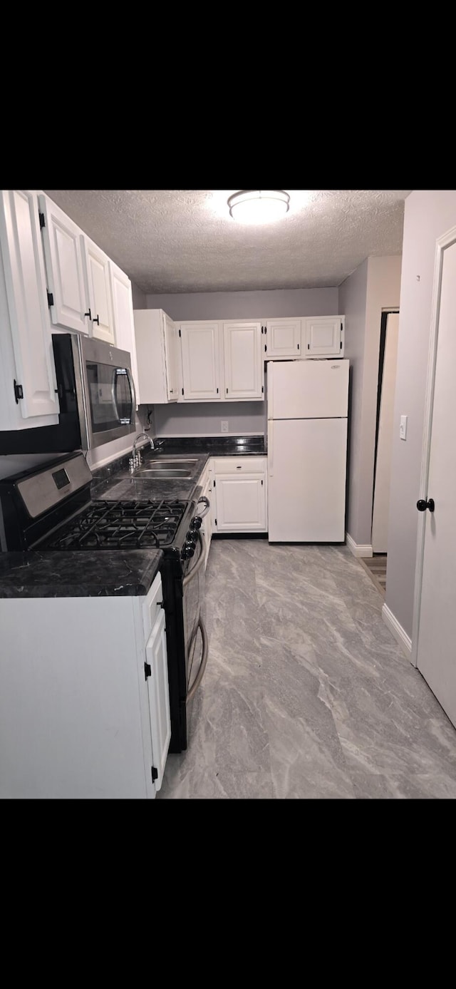 kitchen featuring dark countertops, appliances with stainless steel finishes, a textured ceiling, white cabinetry, and a sink