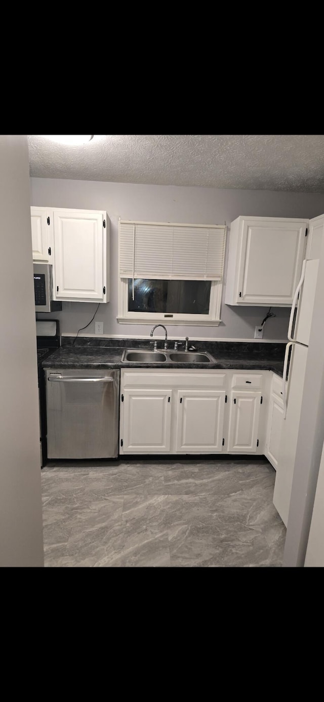 kitchen with dark countertops, appliances with stainless steel finishes, white cabinets, and a sink