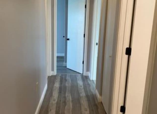 corridor with dark wood-type flooring and baseboards