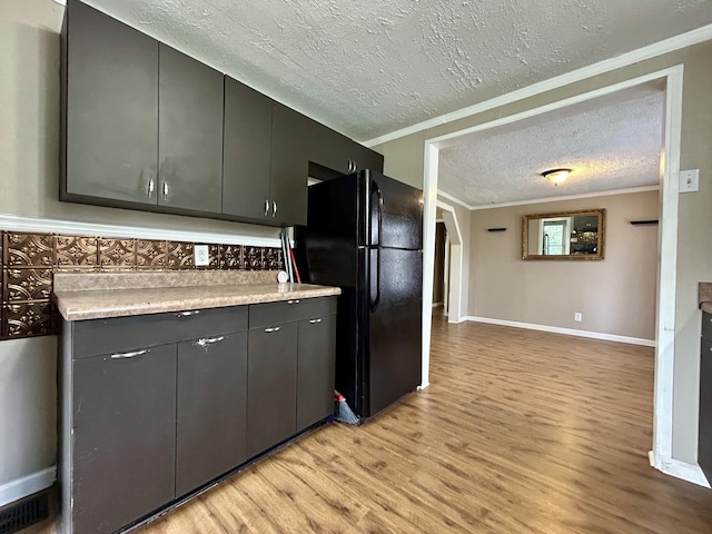 kitchen with ornamental molding, black refrigerator, a textured ceiling, and light wood-type flooring