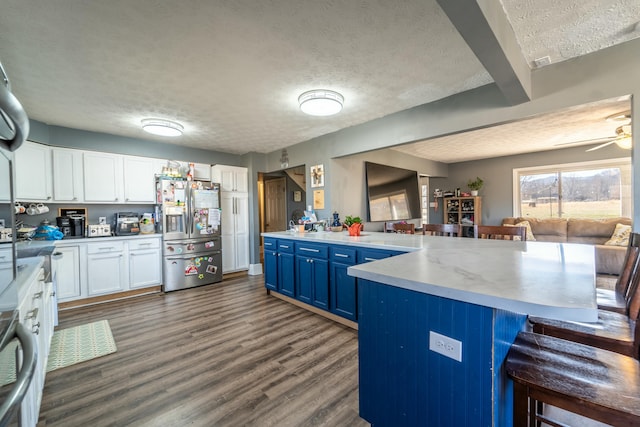 kitchen with blue cabinetry, a kitchen bar, stainless steel fridge, dark hardwood / wood-style flooring, and white cabinets