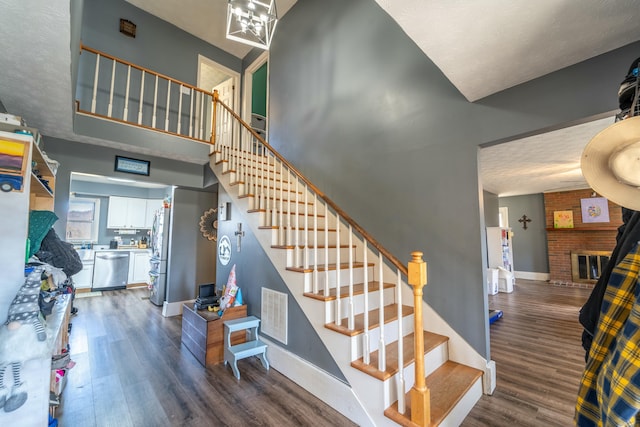 staircase featuring hardwood / wood-style floors, a towering ceiling, a textured ceiling, and a brick fireplace