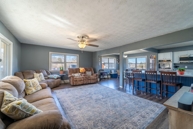 living room featuring dark wood-type flooring, a textured ceiling, and ceiling fan