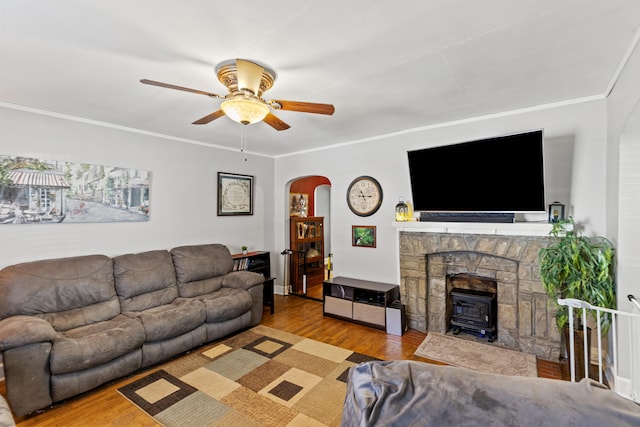 living room featuring ornamental molding, a wood stove, ceiling fan, and light wood-type flooring