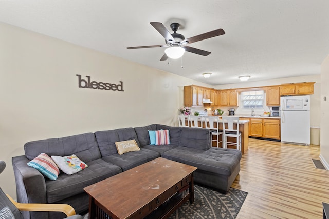 living room featuring ceiling fan, sink, and light hardwood / wood-style floors