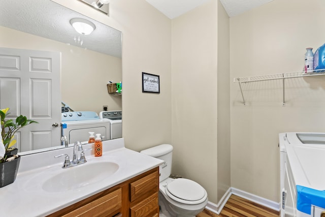 bathroom featuring wood-type flooring, vanity, washer and clothes dryer, toilet, and a textured ceiling