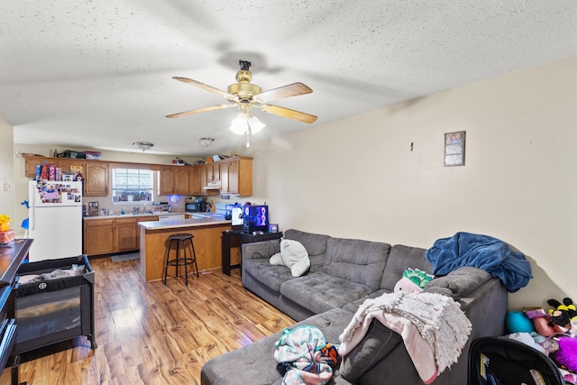 living room with ceiling fan, a textured ceiling, and light wood-type flooring