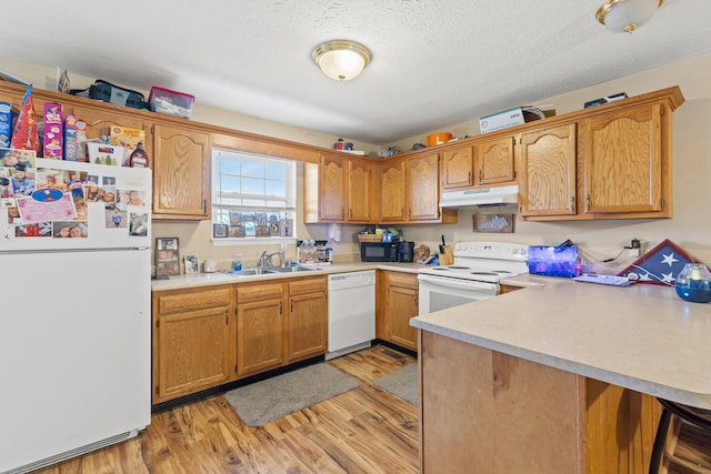 kitchen with white appliances, kitchen peninsula, sink, and light wood-type flooring