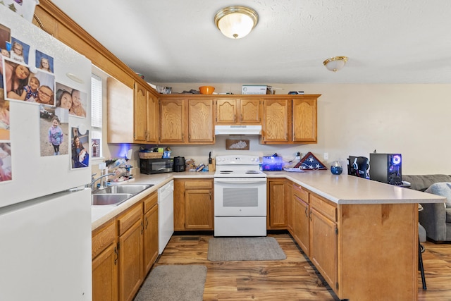 kitchen with a breakfast bar, sink, kitchen peninsula, white appliances, and light hardwood / wood-style floors