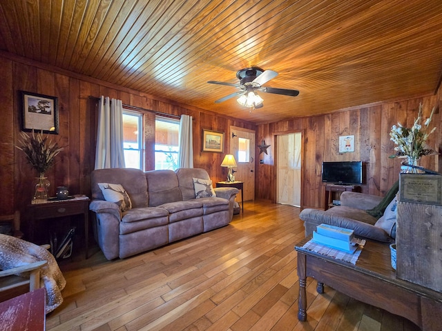 living room with wooden walls, wood ceiling, ceiling fan, and light hardwood / wood-style flooring