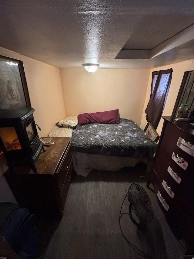 bedroom with a wood stove, a textured ceiling, and dark hardwood / wood-style flooring