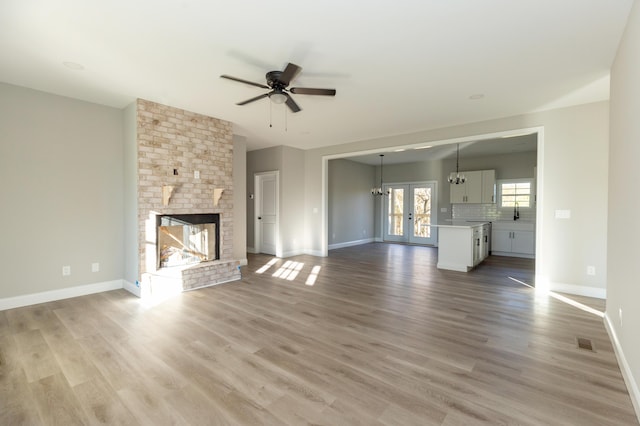 unfurnished living room featuring a brick fireplace, light hardwood / wood-style flooring, french doors, and ceiling fan