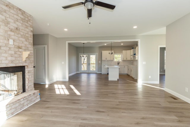 unfurnished living room featuring a brick fireplace, ceiling fan with notable chandelier, light hardwood / wood-style flooring, and sink