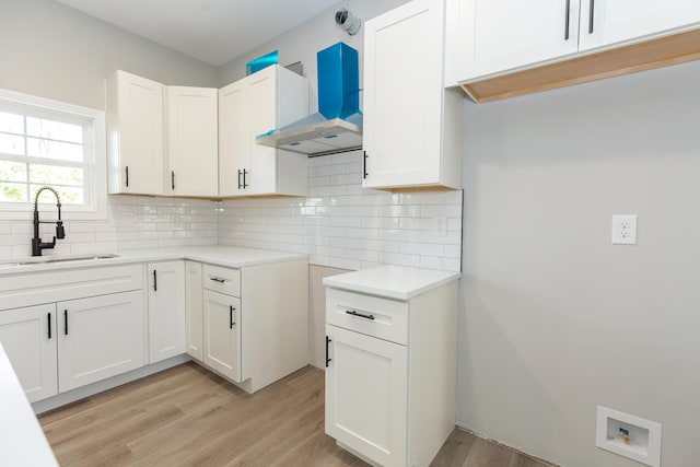 kitchen featuring sink, backsplash, wall chimney exhaust hood, and white cabinets