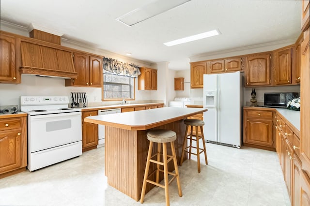 kitchen with white appliances, washer and clothes dryer, a breakfast bar area, ornamental molding, and a kitchen island