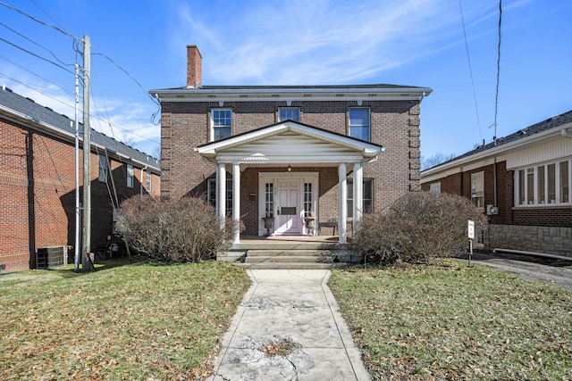 view of front of house featuring central AC unit, a chimney, covered porch, a front lawn, and brick siding