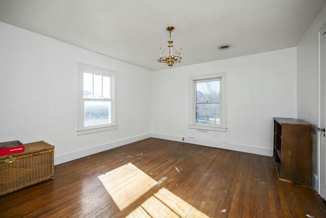 spare room with an inviting chandelier, dark wood finished floors, visible vents, and baseboards