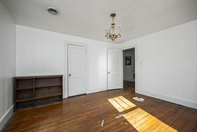 spare room with dark wood-style floors, a notable chandelier, visible vents, and baseboards