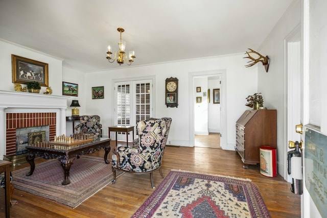 living room with baseboards, ornamental molding, wood finished floors, a brick fireplace, and a notable chandelier