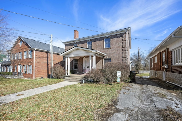 view of front of house featuring covered porch, brick siding, a front lawn, and a chimney