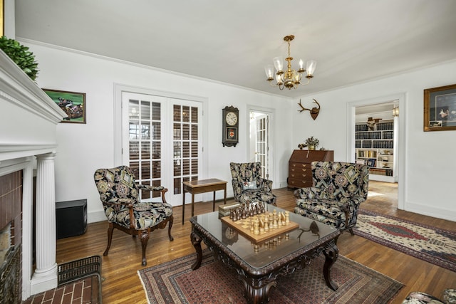 living area with ornamental molding, wood finished floors, a fireplace with flush hearth, and a notable chandelier