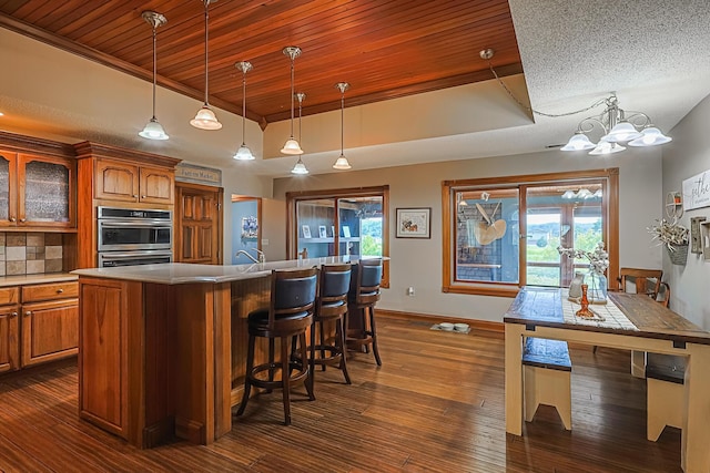 kitchen featuring double oven, decorative light fixtures, dark hardwood / wood-style flooring, a kitchen island with sink, and a tray ceiling