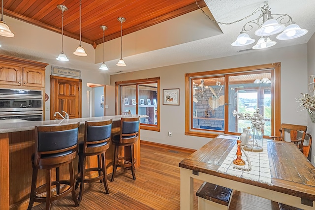 kitchen with a tray ceiling, light hardwood / wood-style floors, double oven, and hanging light fixtures