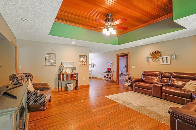 living room featuring wood ceiling, light hardwood / wood-style flooring, a textured ceiling, a tray ceiling, and ceiling fan