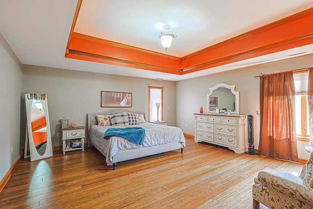 bedroom with multiple windows, a tray ceiling, light hardwood / wood-style floors, and crown molding