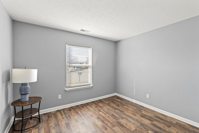 unfurnished room featuring dark wood-type flooring and a textured ceiling